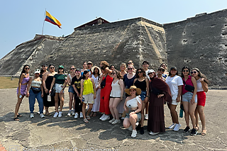 nursing students standing in front of an old colombian fortress with a yellow, blue and red flag flapping above them