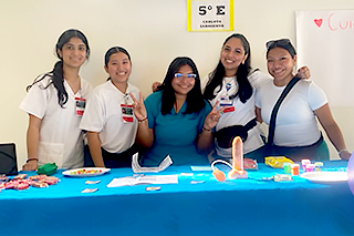 nursing students standing behind blue table, smiling