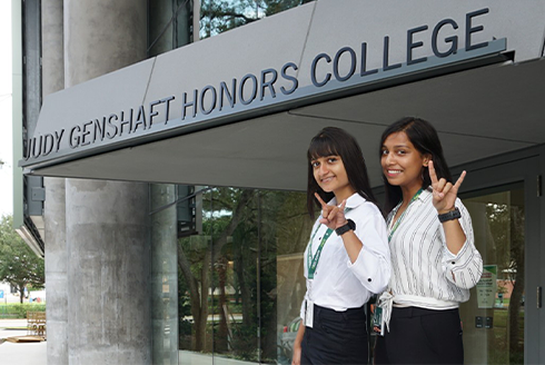 Two people smiling in front of the Judy Genshaft Honors College