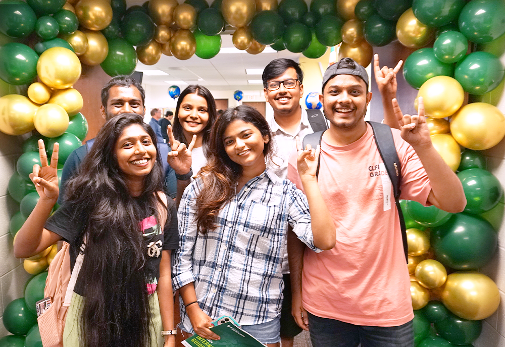 Students smiling with gold and green balloons framing the background