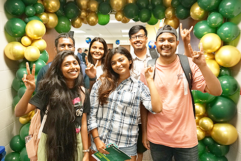 Students smiling with gold and green balloons framing the background