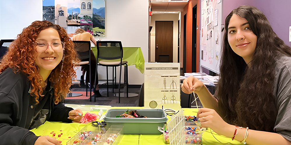 Two students smiling while making bead bracelets