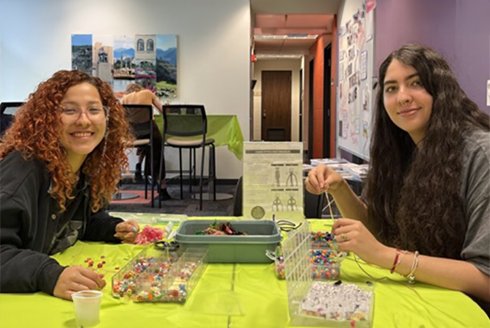 Two students smiling while making bead bracelets