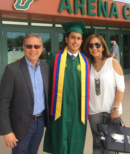 Julian Escallon in his green USF graduation regalia standing between his parents