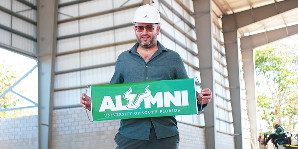 Rene Jacir posing with a USF green banner that says "Alumni"