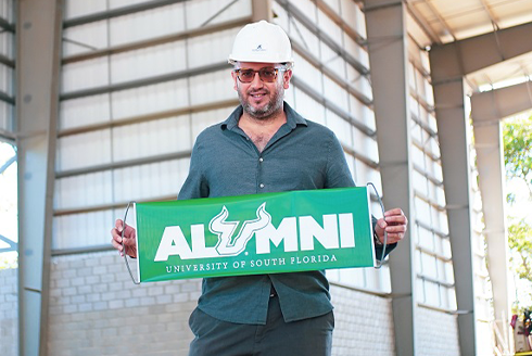 Rene Jacir posing with a USF green banner that says 