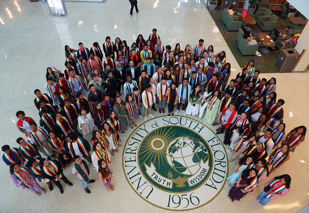 A group of graduating international students looking up and smiling at camera from SMC lobby