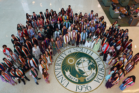 A group of graduating international students looking up and smiling at camera from SMC lobby