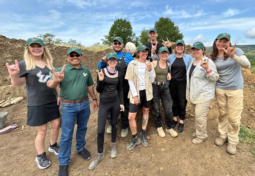 Students, Bethard, Dr. Kiki Caruson, and Provost Mohapatra stand at Transylvania burial site raising their hands with the bull sign