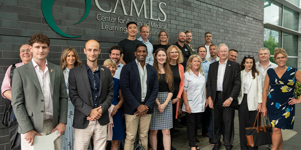 A group of people standing in front of a gray brick building with the logo of CAMLS on it