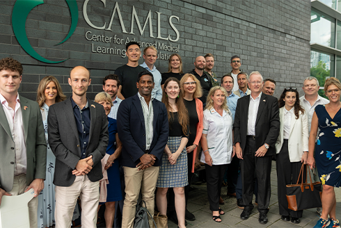 A group of people standing in front of a gray brick building with the logo of CAMLS on it