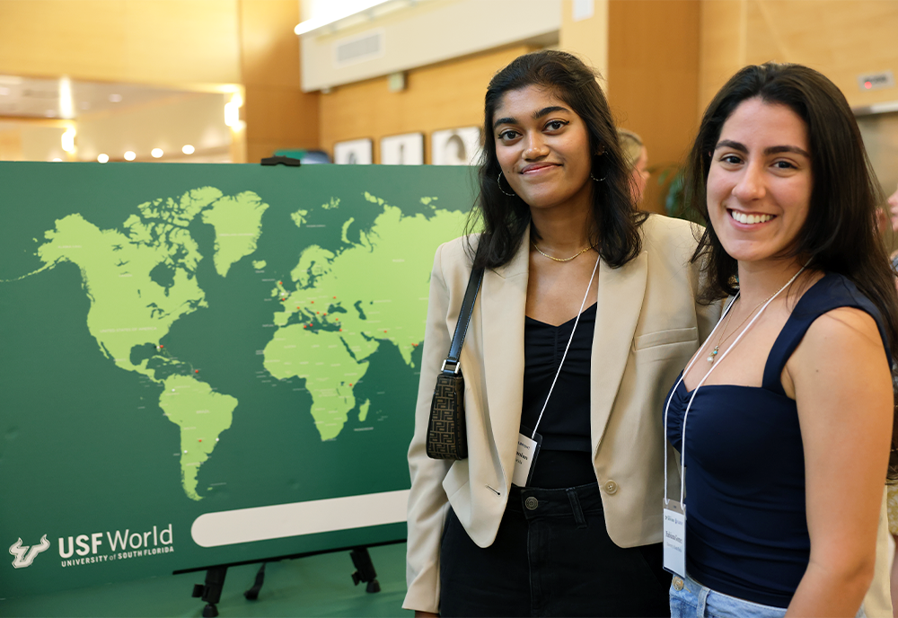 Two people standing by a green map of the world that has "USF World" on the bottom left corner