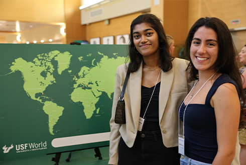 Two people standing by a green map of the world that has 