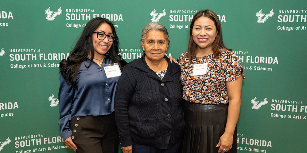 Cielo Gomez with her mom and another person smiling with a green usf Bulls background