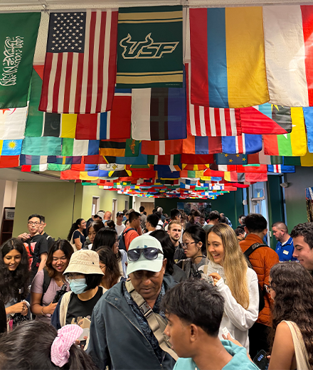 A group of people socializing under flags of different countries that hang from the ceiling