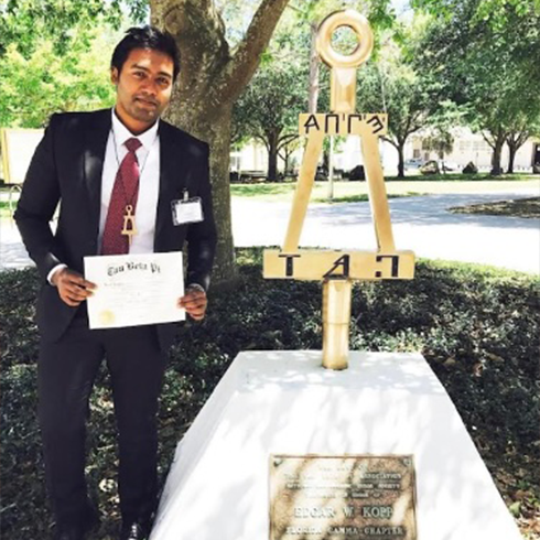 khan holding a document by an honors society statue