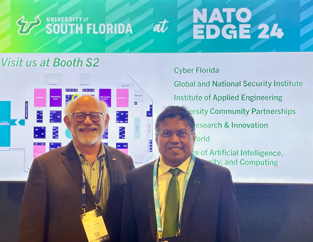 Provost and Dr. Eisenberg stand together in front of a screen that has a slide from Nato Edge 24