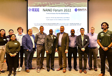 Nirmita and a group of professionally dressed people posing in front of a projector with the name "NANO Forum 2022"