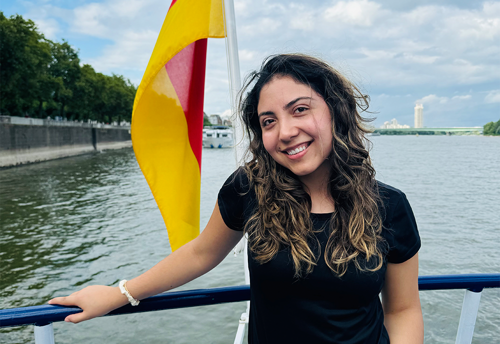 Olga posing in front of a German flag hanging off the side of a boat and over the water