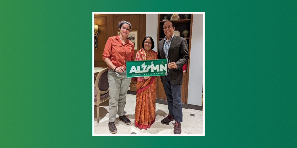 Alum Ranvir Singh poses with two women and holding a banner that says "Alumni"