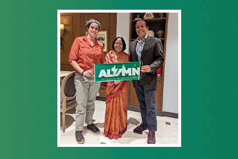 Alum Ranvir Singh poses with two women and holding a banner that says 