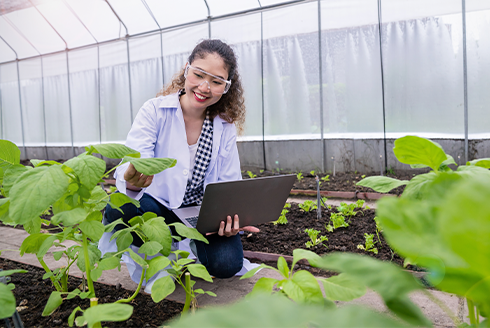 A student scientist studying a plant in a greenhouse