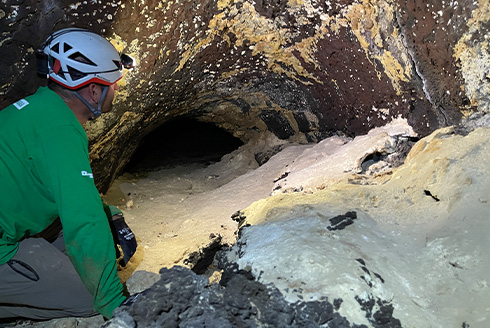 A man with protective helmet and light is looking into a cave