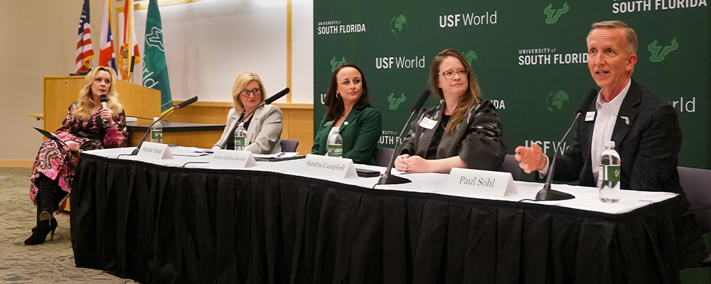 Panelists sitting in front of a USF World step and repeat banner