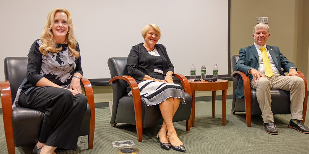 Dr. Caruson, Stephenson, and General McKenzie, Jr are sitting in chairs on a stage for a presentation