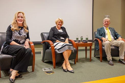 Dr. Caruson, Stephenson, and General McKenzie, Jr are sitting in chairs on a stage for a presentation