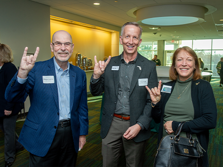 A group of three people smiling and holding up "bulls sign" with their hands