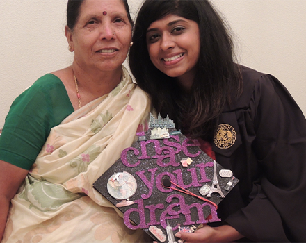 Neha with another woman holding a graduate cap that is decorated with purple words that say "Chas your dream"