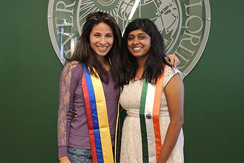 Neha standing beside another person, both wearing sashes with the flag colors of their home countries