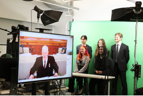 Five Honors students stand in front of a green screen while listening to Right Honorable Sir Lindsay Hoyle from a monitor.