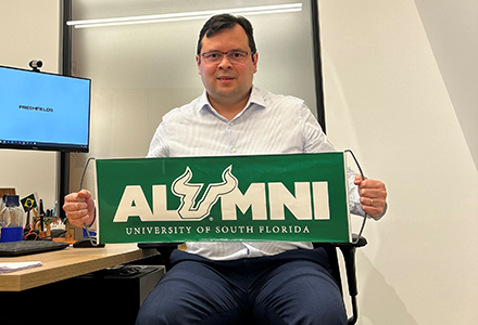 an alumnus holding a green sign with the word "Alumni" on it